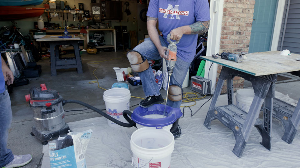 man mixing material in a bucket with an eggbeater mixer